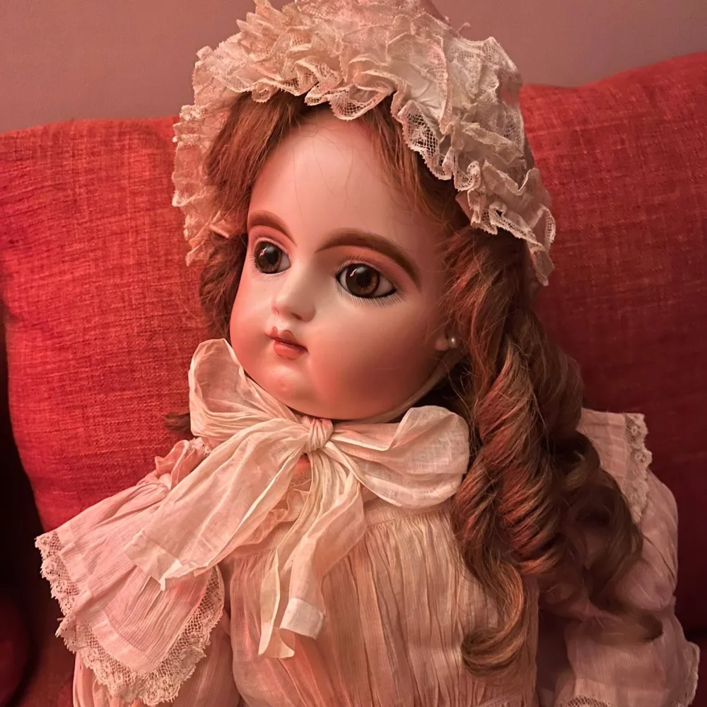 Close detail of an antique bisque doll's face showing painted lashes, feathered brows and a closed mouth.