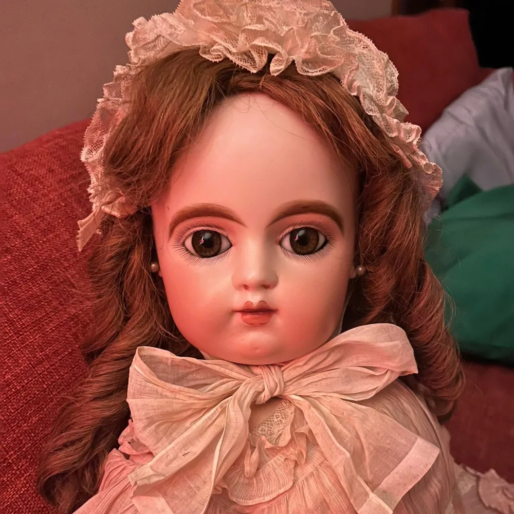 Antique French bébé with brown paperweight eyes, auburn mohair wig and a lace-trimmed bonnet.