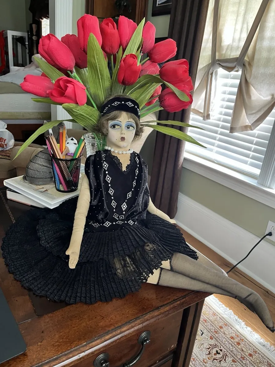 Boudoir Gerling doll seated in a black outfit beside red tulips, full view.